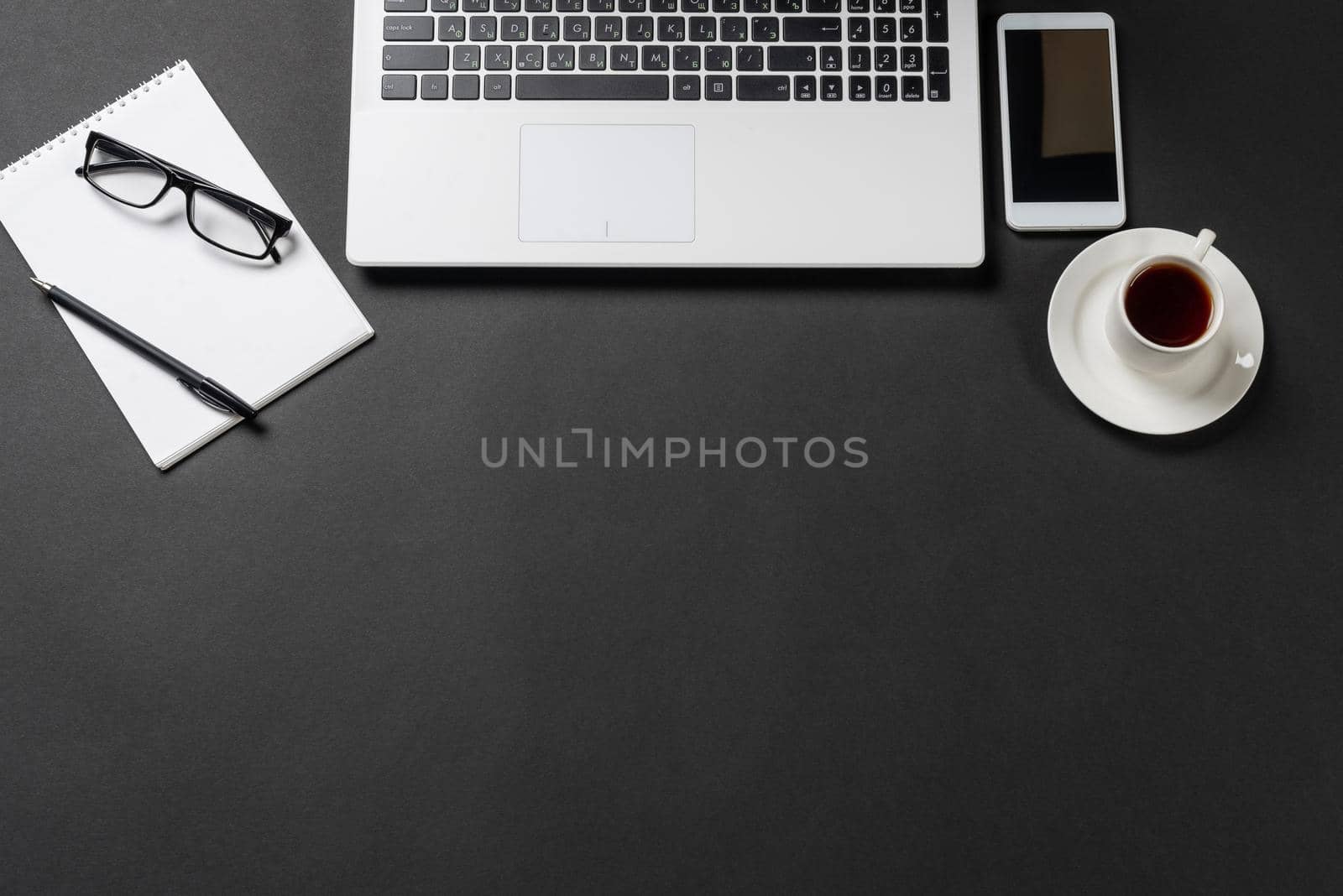 Top view of office workplace with digital gadgets. Flat lay black surface with computer keyboard, smartphone and notebook. Top view coworking workspace and freelance. Digital technology and mobility.