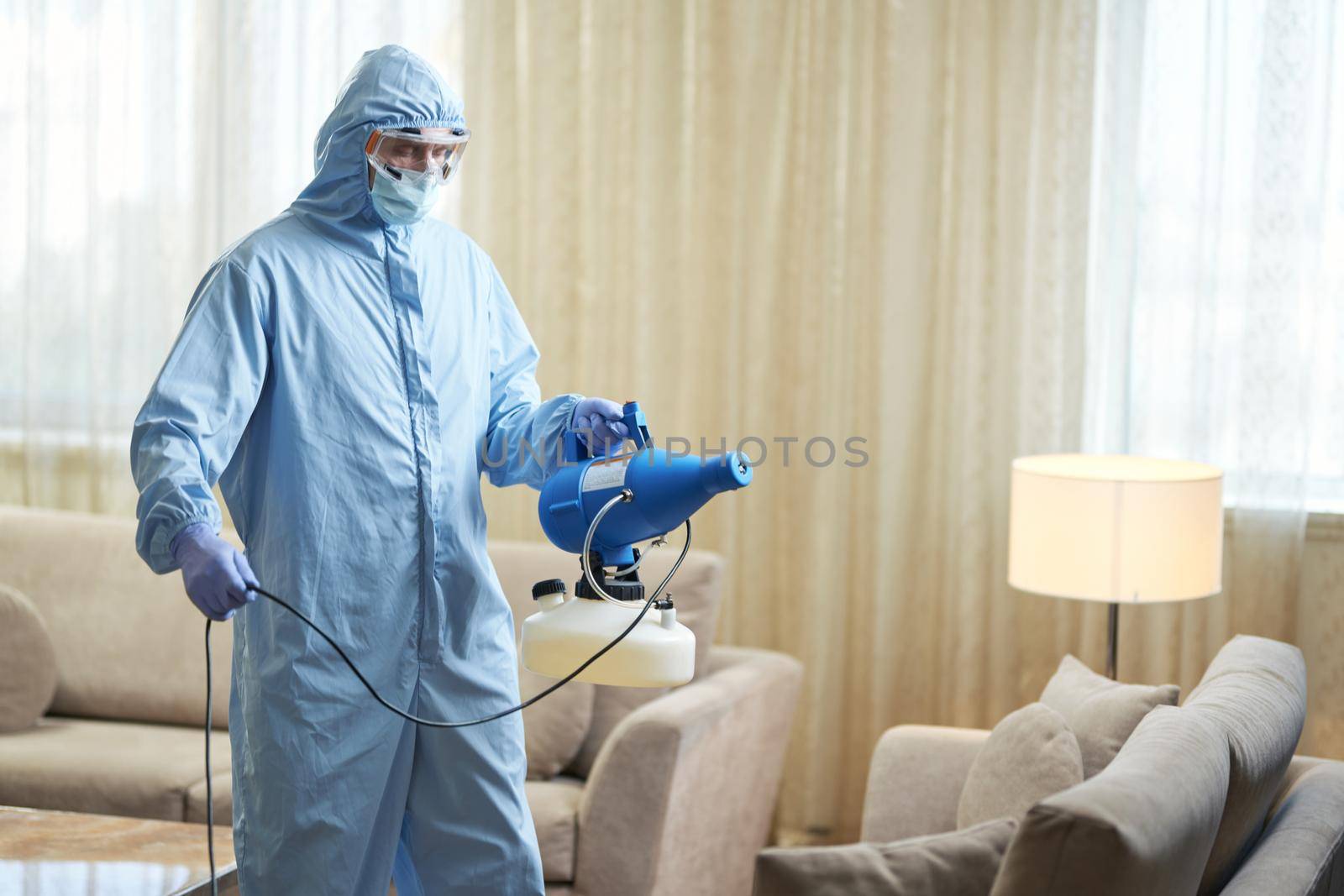 Worker wearing protective overalls and disinfecting a hotel apartment Coronavirus and quarantine concept