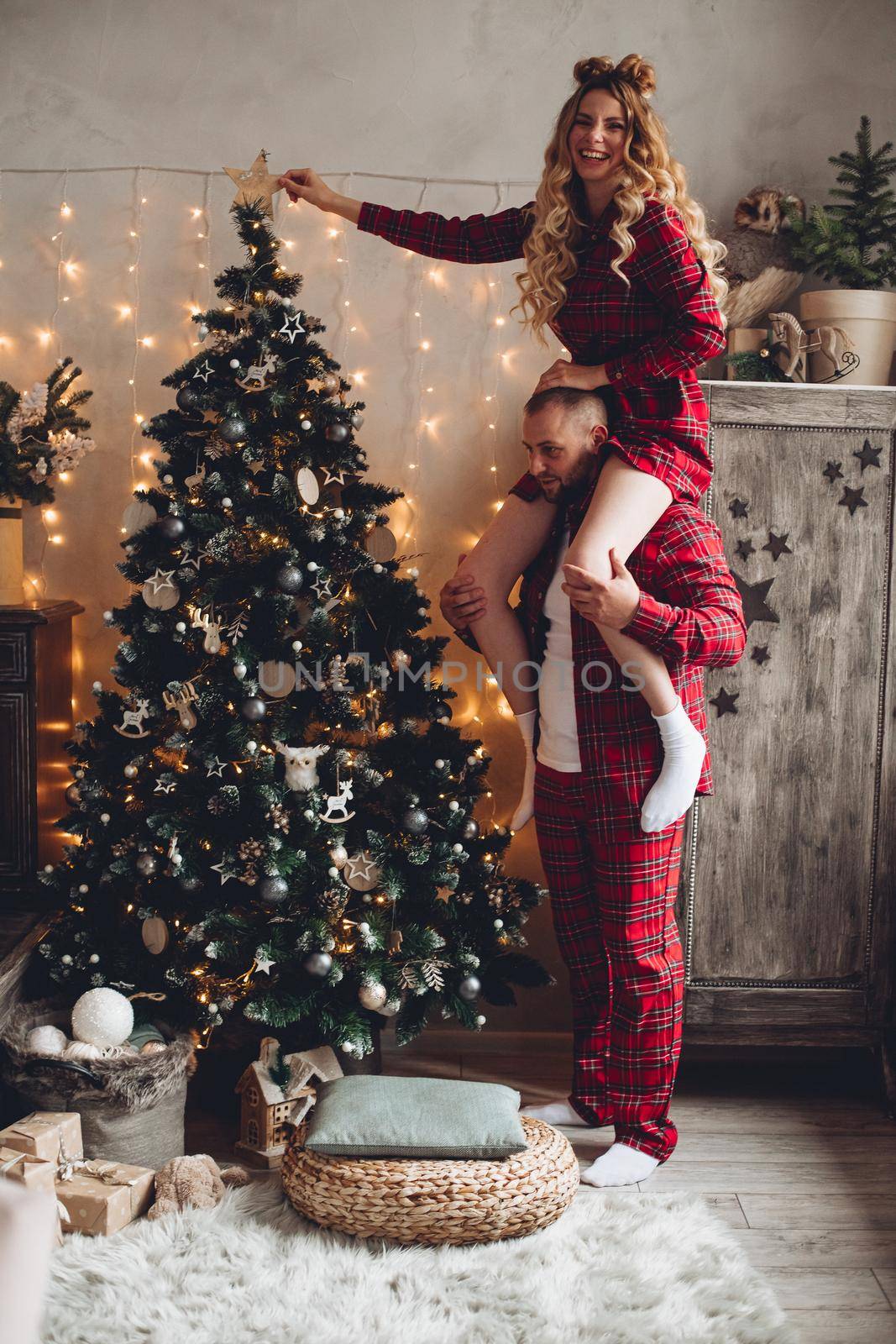 Beautiful young woman decorating a christmas tree and sitting on her husband shoulders