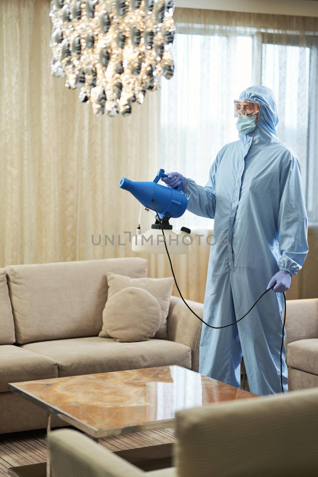 Worker in blue chemical protection suit doing disinfection and spraying of room. Coronavirus and quarantine concept
