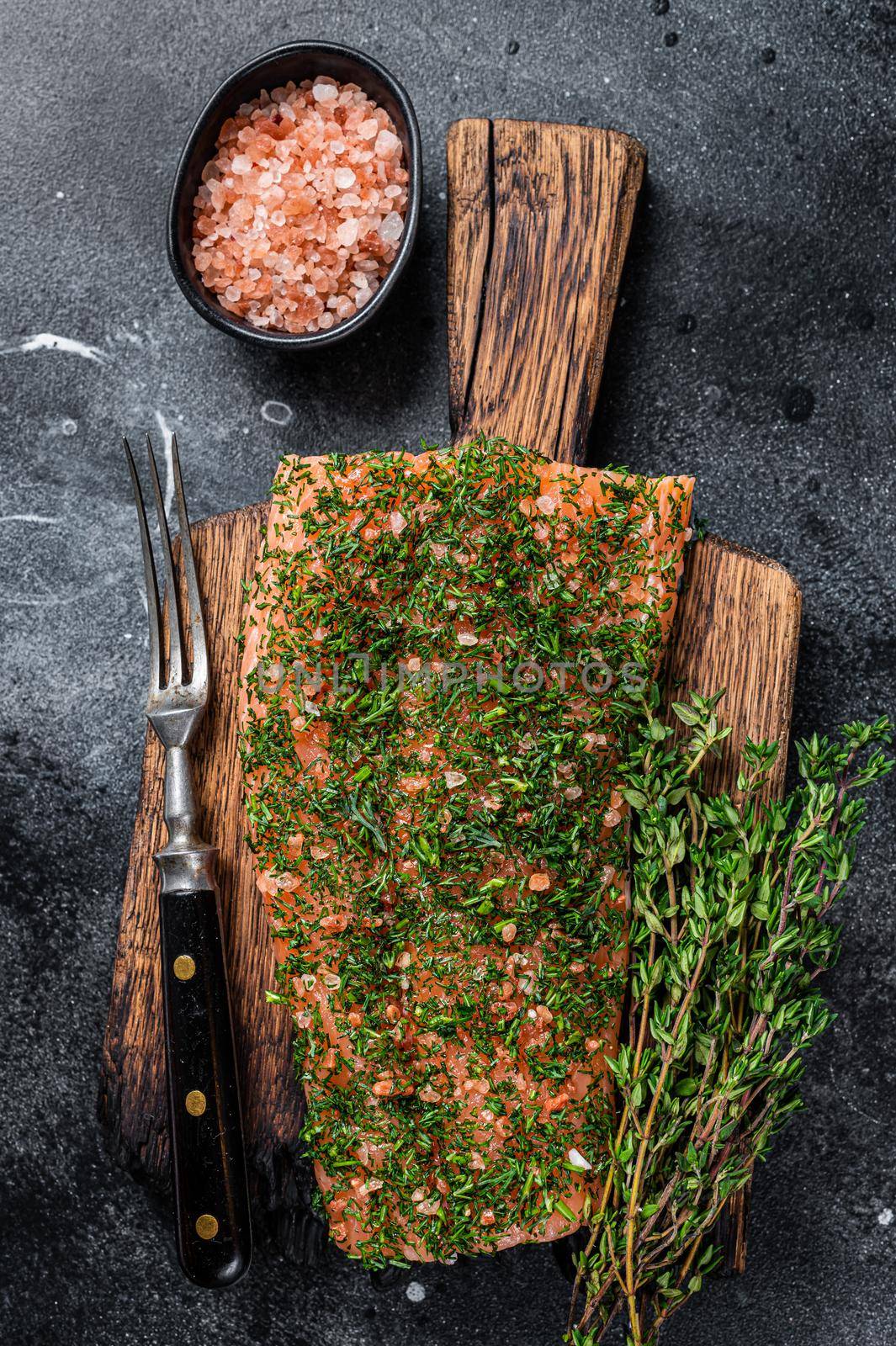 Gravlax cured salmon with dill and salt on wooden board. Black background. Top view by Composter