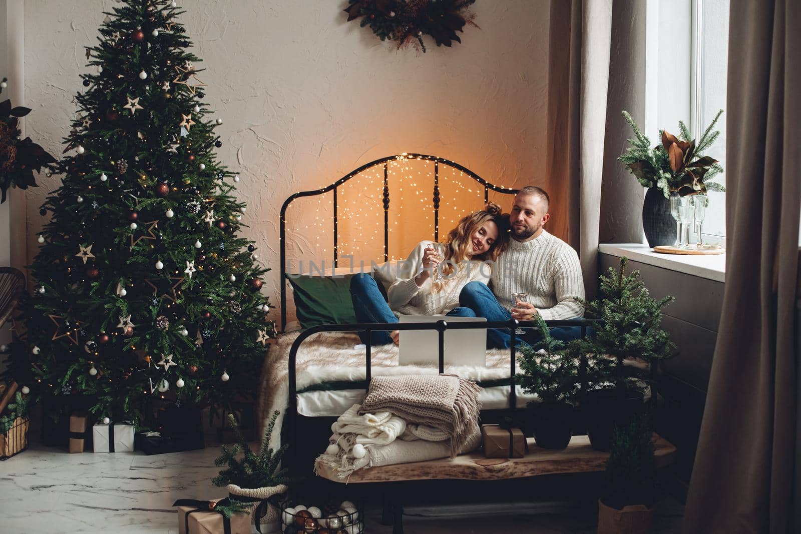 Cheerful young couple with glasses of champagne celebrating Christmas or New Year via laptop.