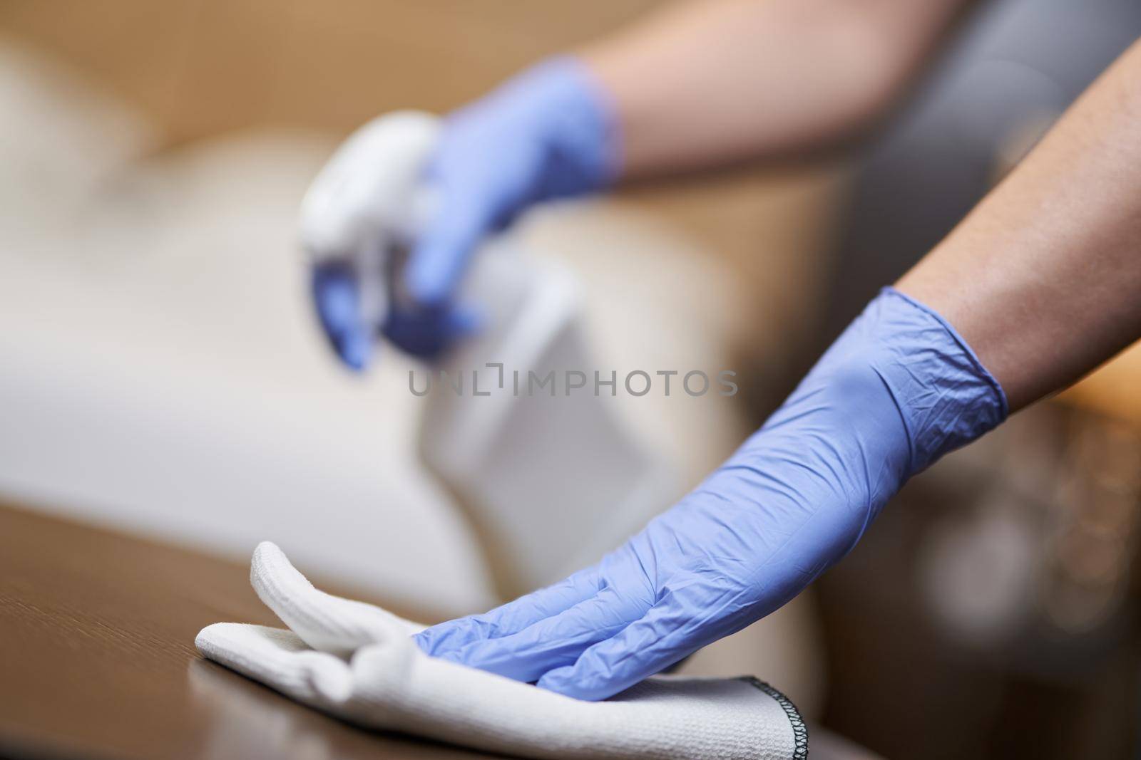 Cropped photo of maid cleaning and polishing wooden table with a spray detergent. Housekeeping and hygiene concept