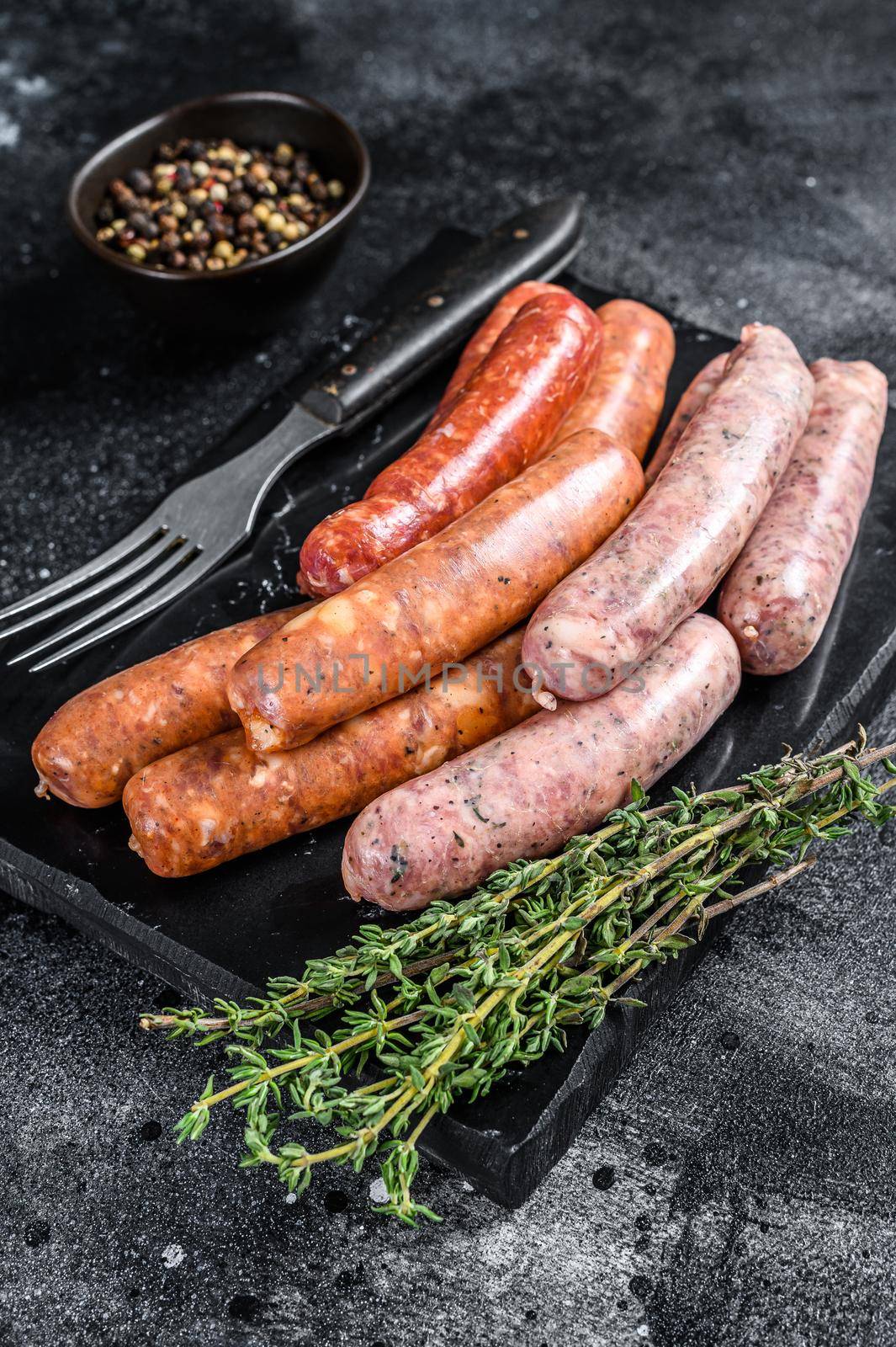 Assorted raw homemade sausages on a stone board. Black background. Top view.