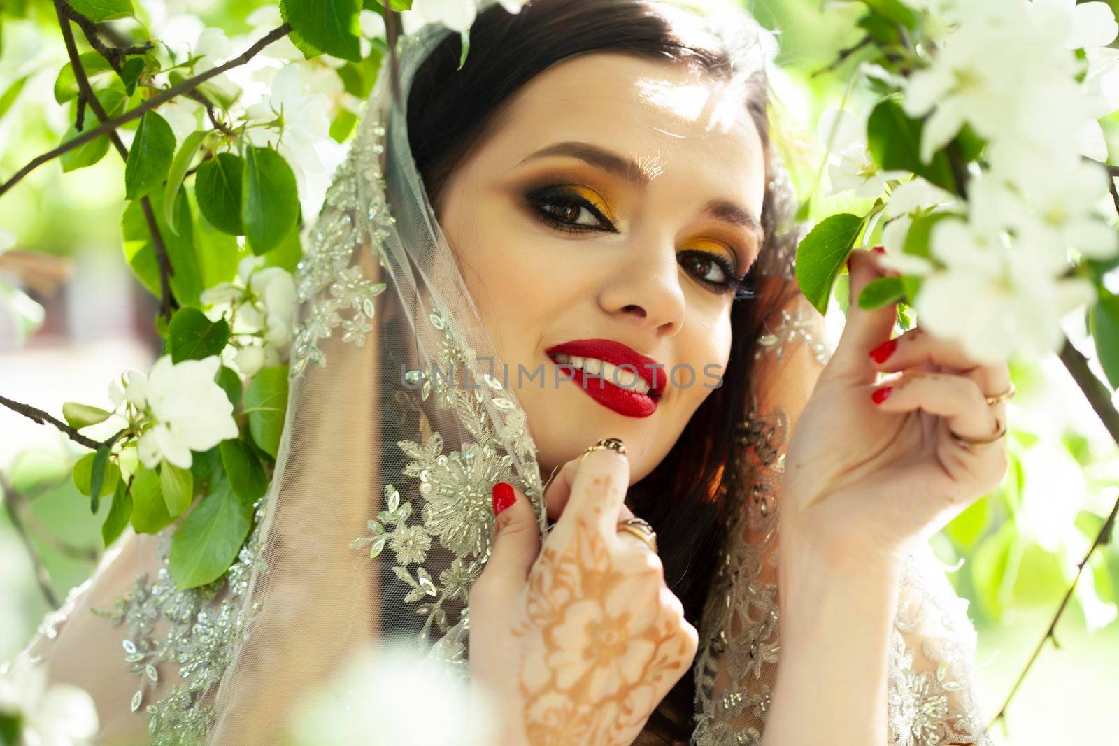 young pretty indian girl in jewelry and veil posing cheerful happy smiling in green park, lifestyle people concept close up