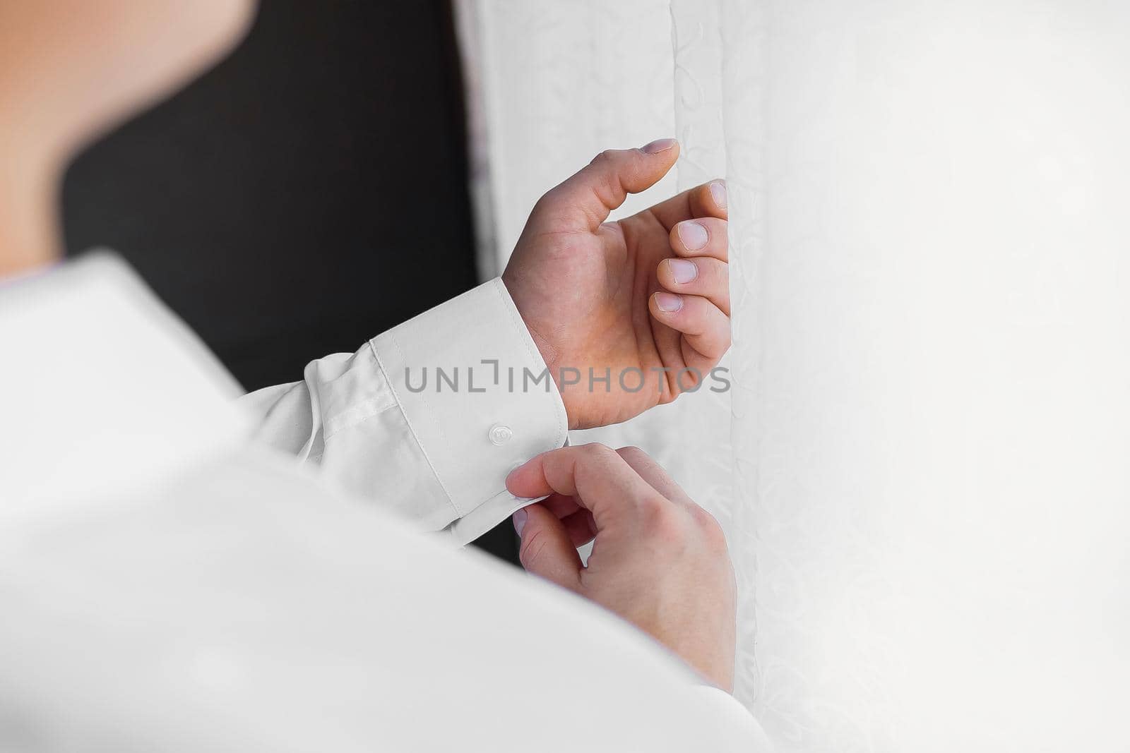 A man in a white shirt clasps his sleeves standing by the light from the window by AYDO8