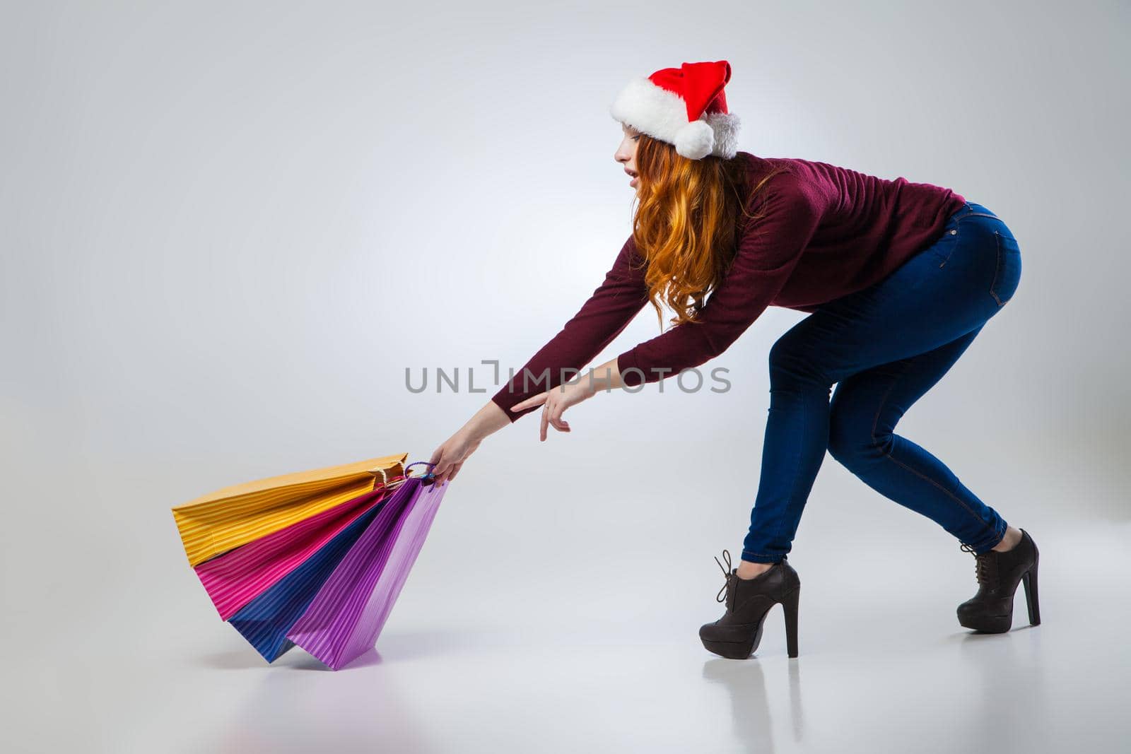 beautiful young girl in winter hat with colorful shopping bags over gray background,