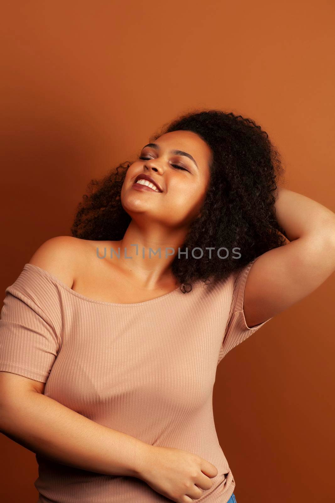 pretty young african american woman with curly hair posing cheerful gesturing on brown background, lifestyle people concept close up