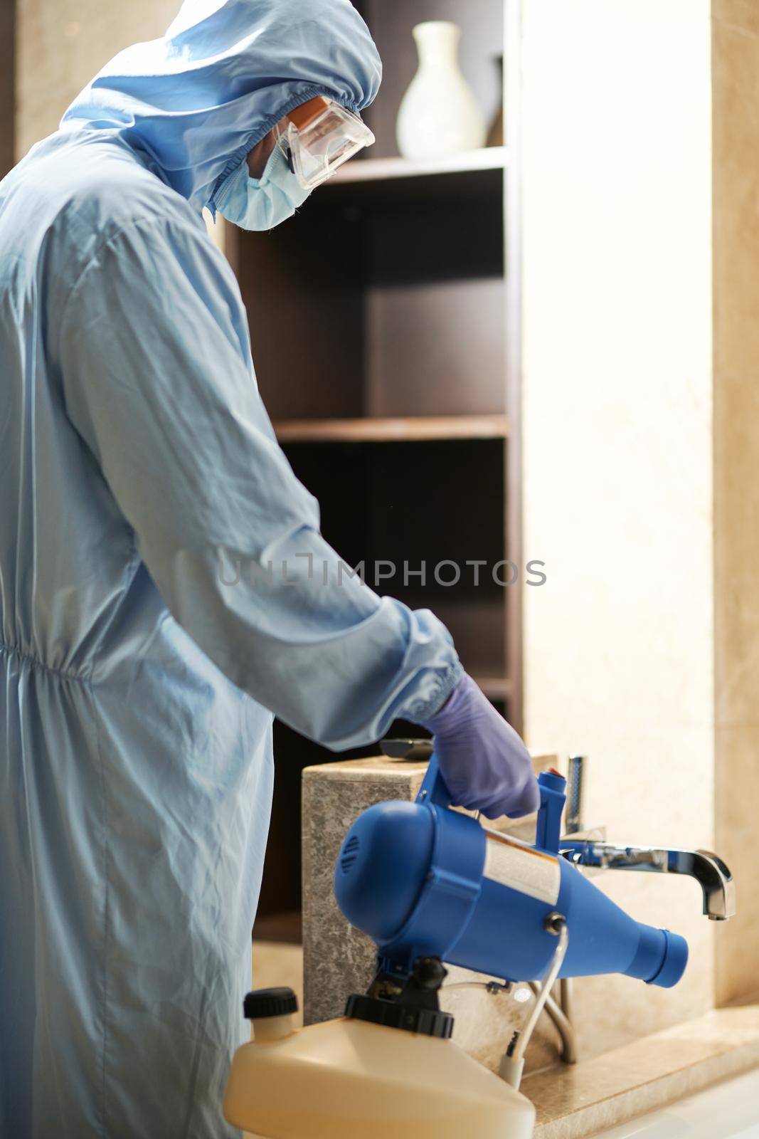 Disinfector in a protective suit and mask spraying disinfectants in hotel bathroom. Coronavirus and quarantine concept