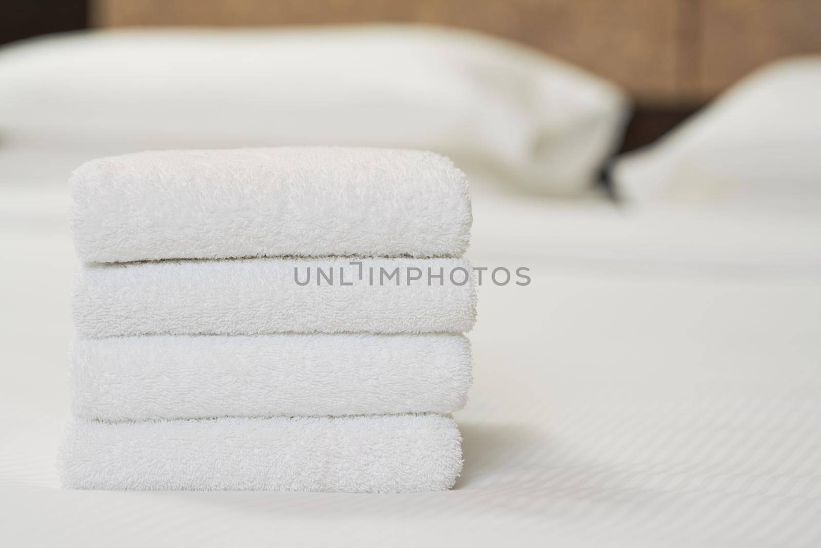 White clean towels stacked on bed in bedroom by friendsstock