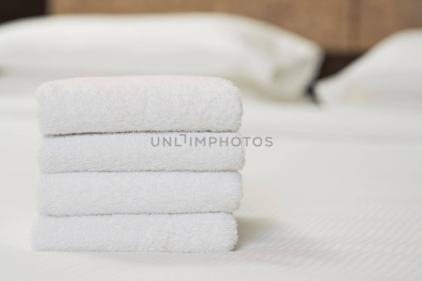 Close up of four white towels on bed in hotel room for customer. Copy space. Hotel service concept