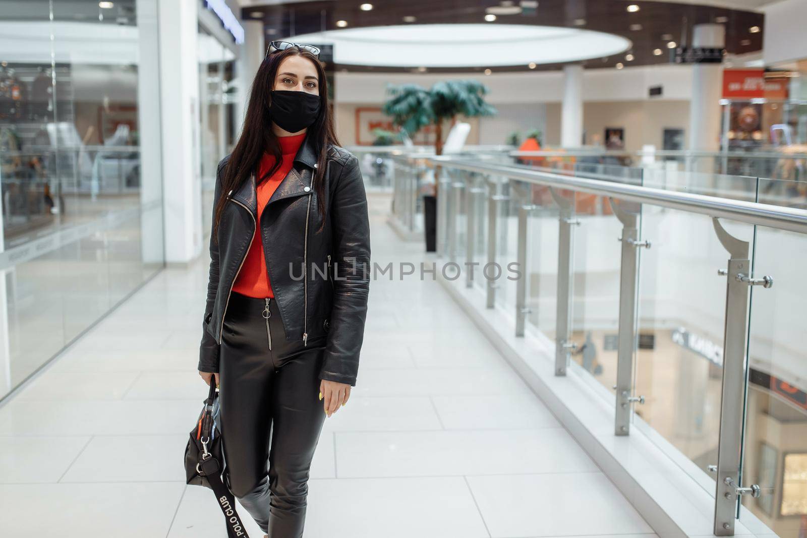 A girl with a medical black mask is walking along a shopping center. Coronavirus pandemic. A woman with a mask is standing in a shopping center. A girl in a protective mask is shopping at the mall.