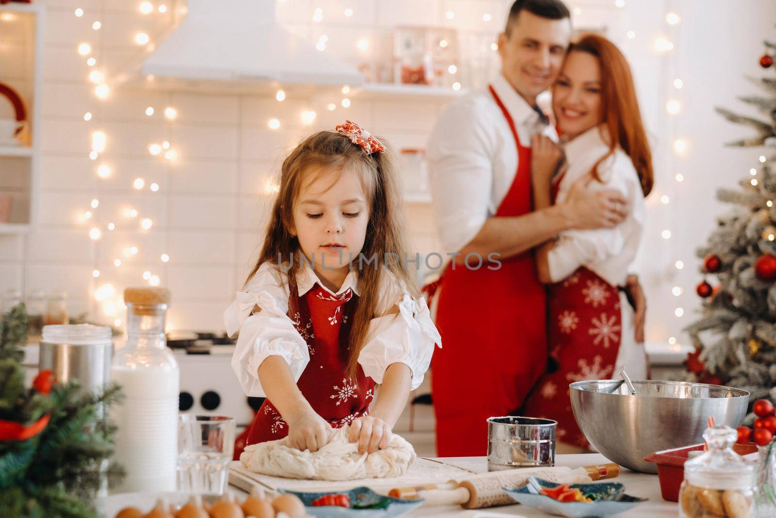 A little girl in the New Year's kitchen makes dough, and her mom and dad are watching next to her by Lobachad