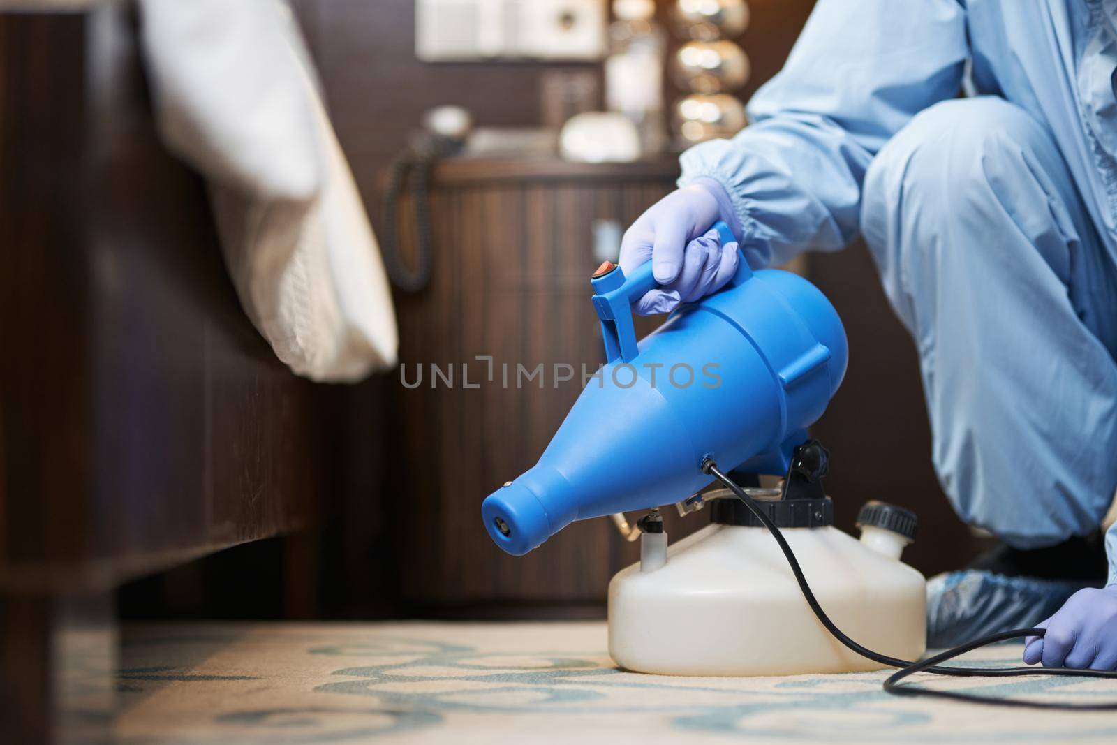 Cropped photo of man in sterile uniform, with gloves and mask holding sprayer in room. Coronavirus and quarantine concept