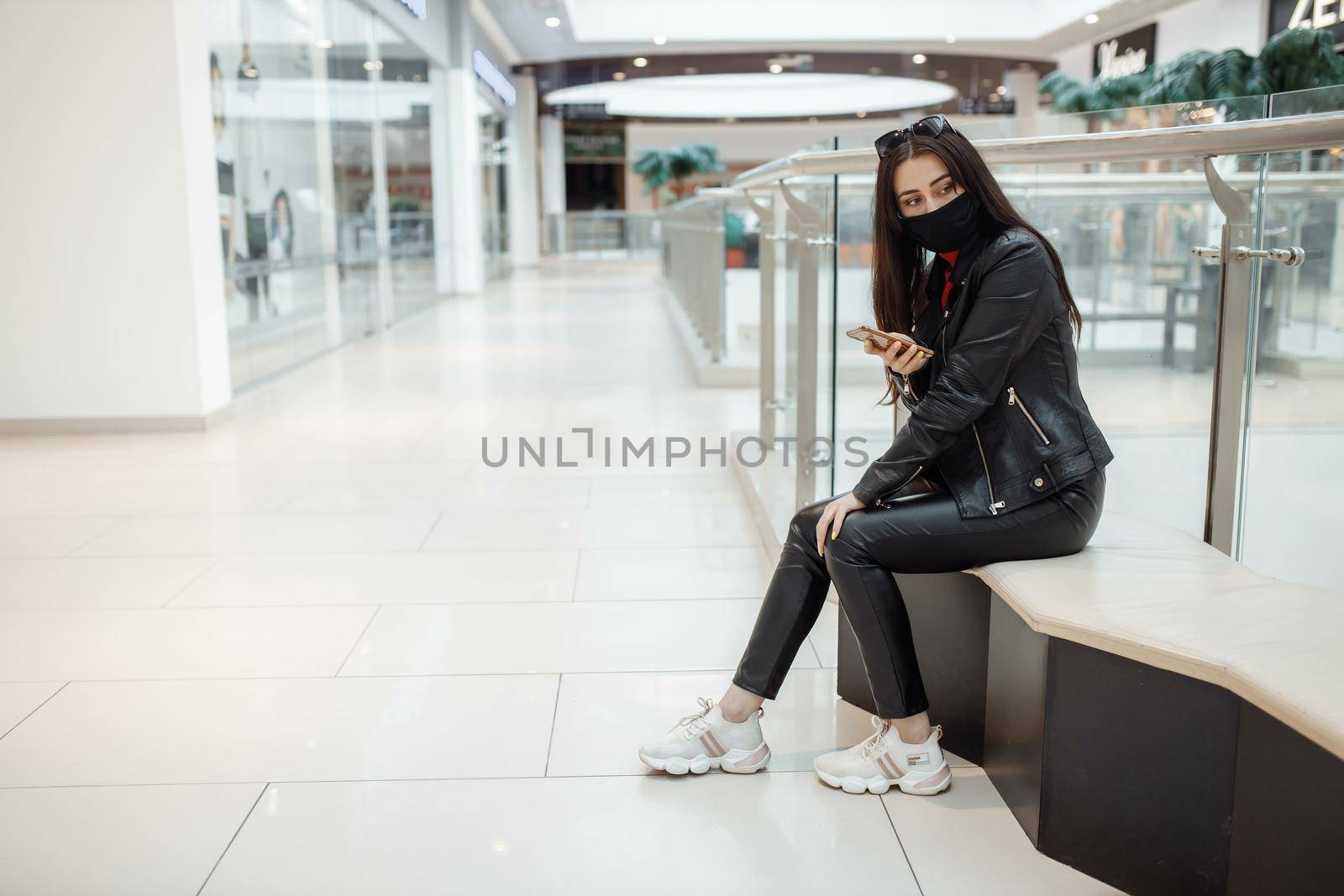 Girl with medical black mask and mobile phone in a shopping center. Coronavirus pandemic. A woman with a mask is standing in a shopping center by UcheaD