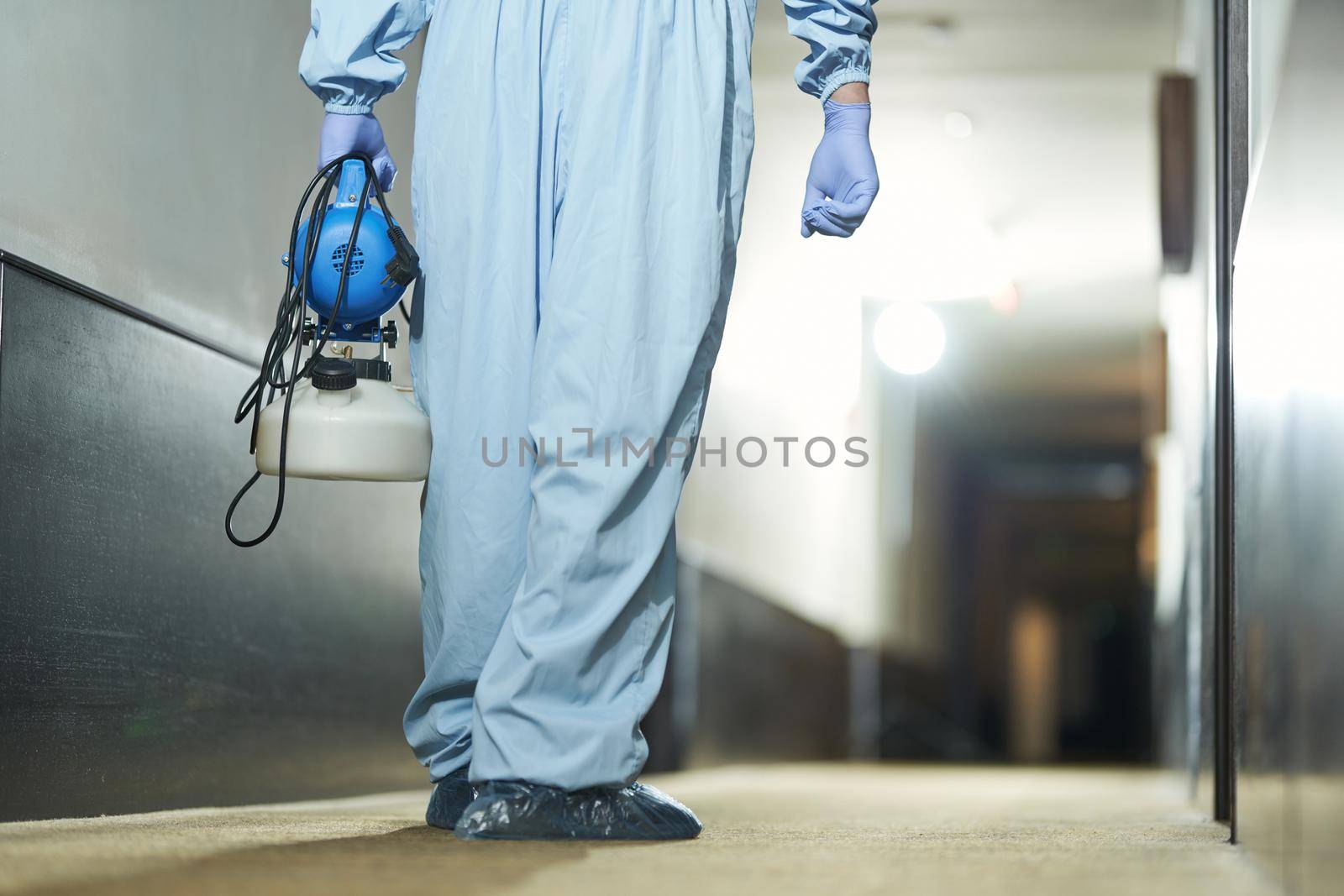 Back view of sanitary worker using sprays for remove bacteria from the surface in hotel. Coronavirus and quarantine concept
