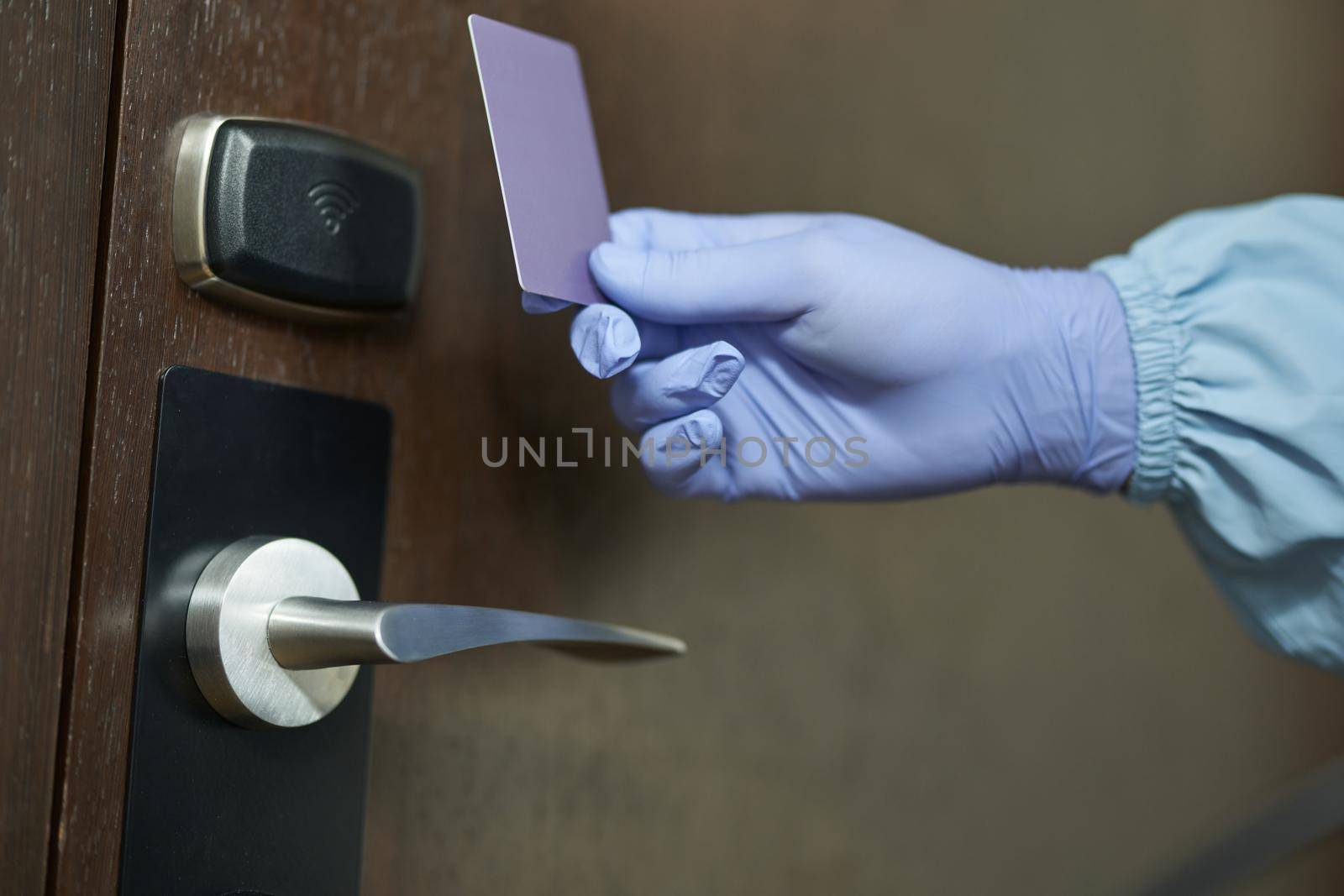 Close up of worker in blue suit and protective gloves holding card in front of the door to the room. Coronavirus and quarantine concept