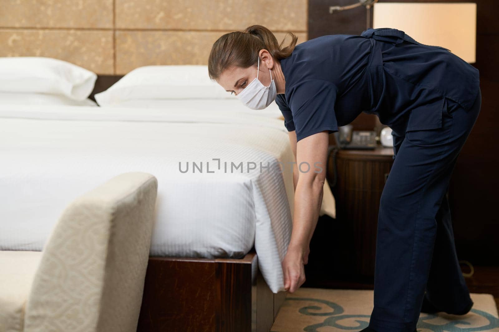 Caucasian maid wearing mask and cleaning bed in luxury hotel room Hotel service concept