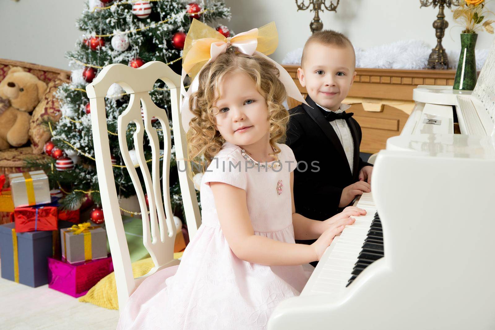 Solemnly dressed little boy and girl into the night, sitting at a white piano. Children put hands on the keys.