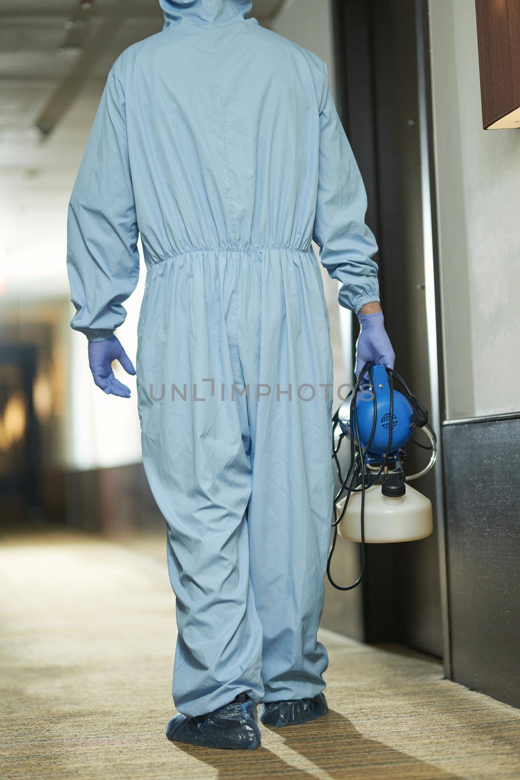 Back view of male specialist in blue suit with disinfectant going to sanitize room in hotel. Coronavirus and quarantine concept