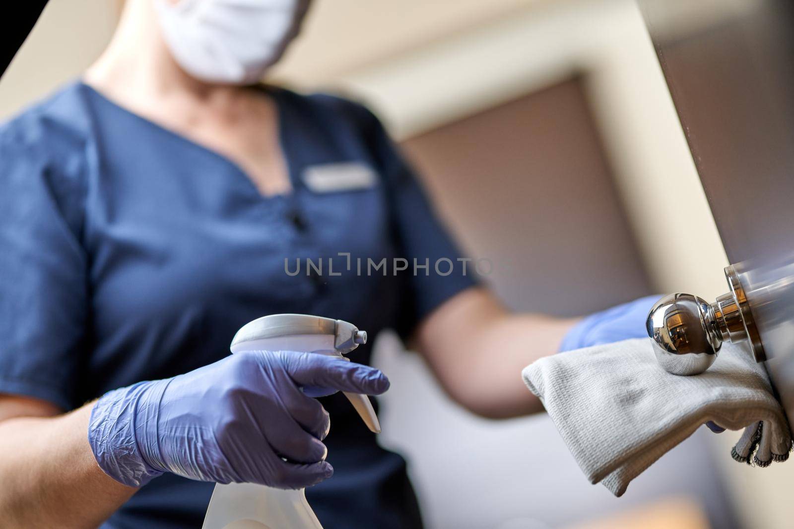 Cropped photo of chambermaid wearing gloves and wiping the door handle with a special disinfectant. Hotel service concept