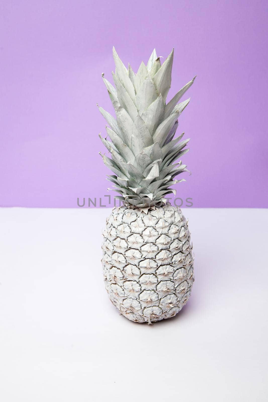 White whole fresh pineapple placed on table in modern studio on violet background