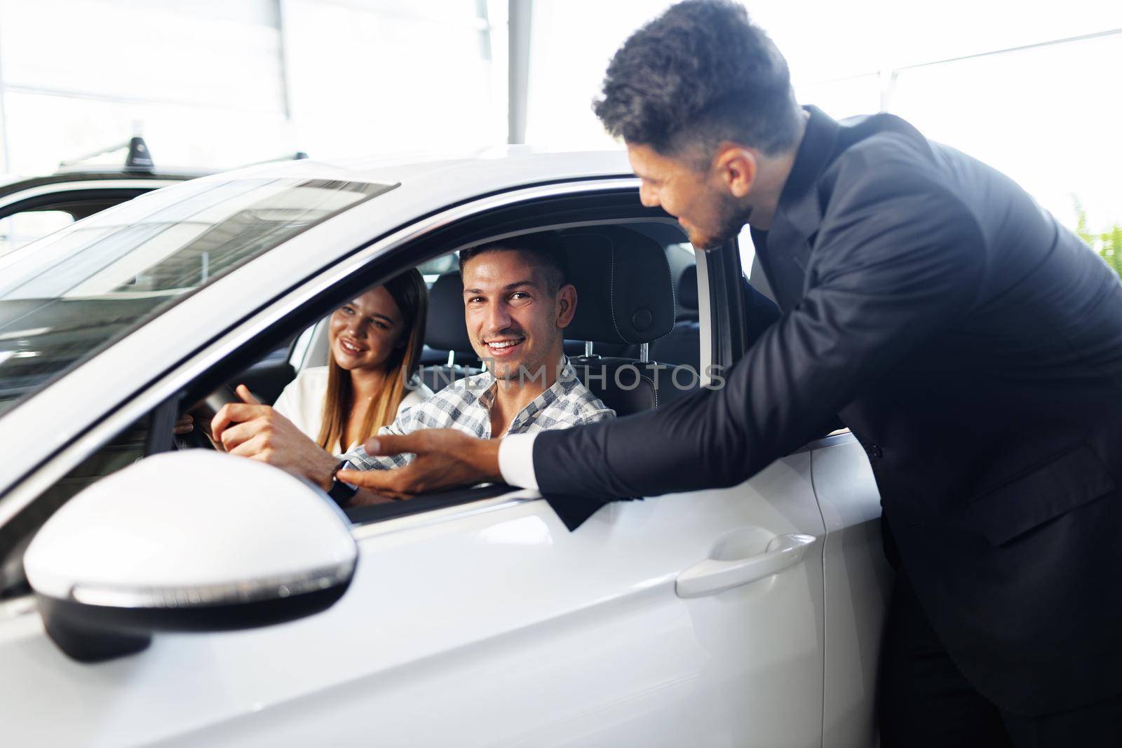 Young couple choosing a car at the dealership with manager helping by Fabrikasimf