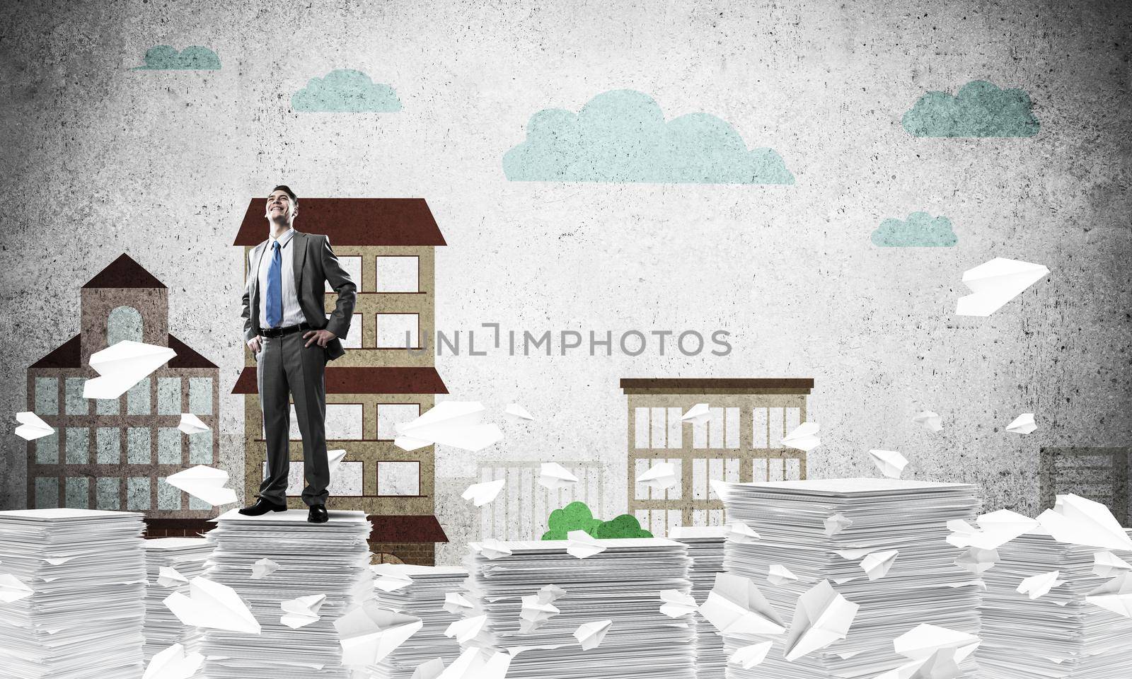 Confident businessman in suit standing on pile of documents among flying paper planes with drawn cityscape background. Mixed media.