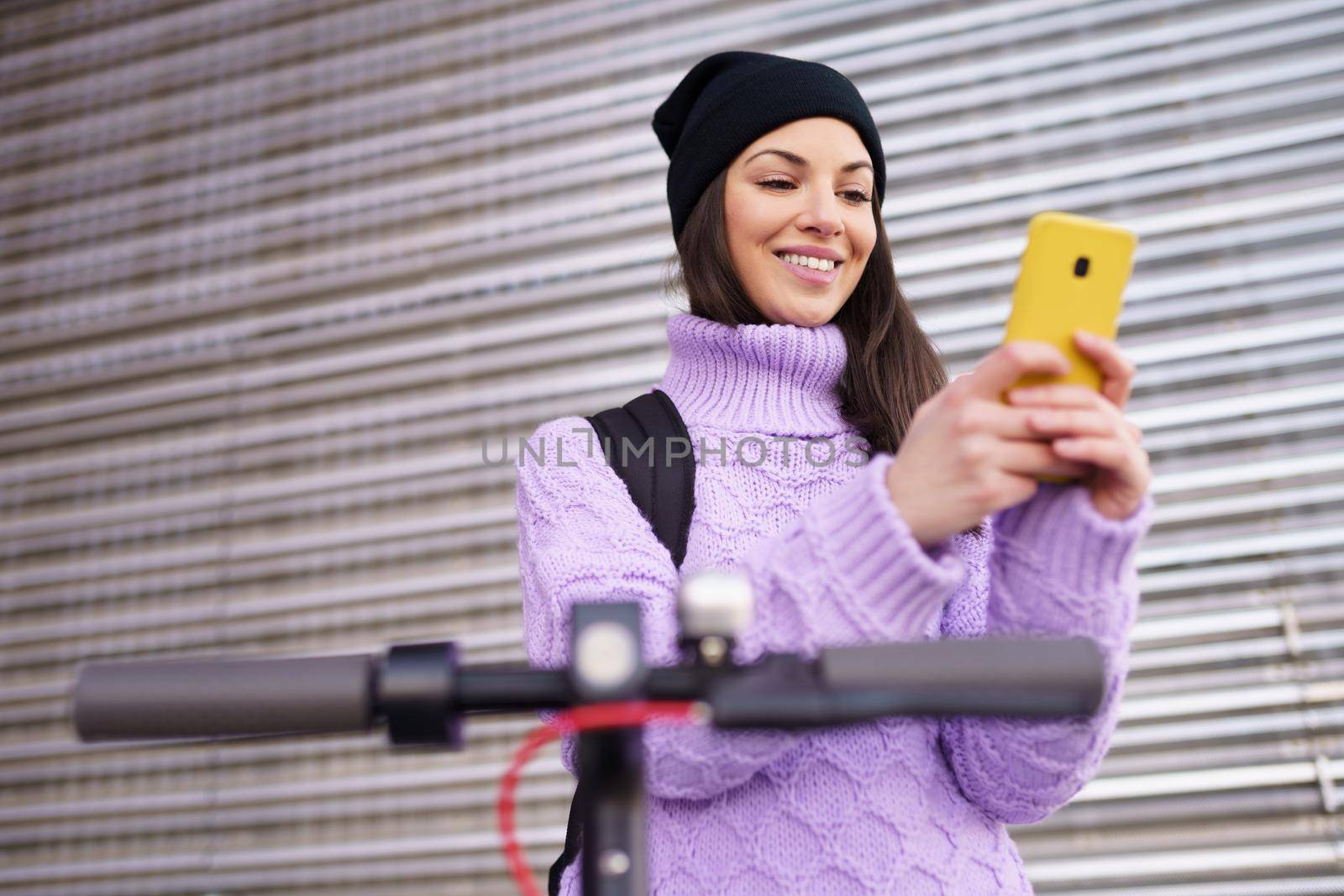 Woman in her twenties with electric scooter using a smartphone outdoors. Lifestyle concept.