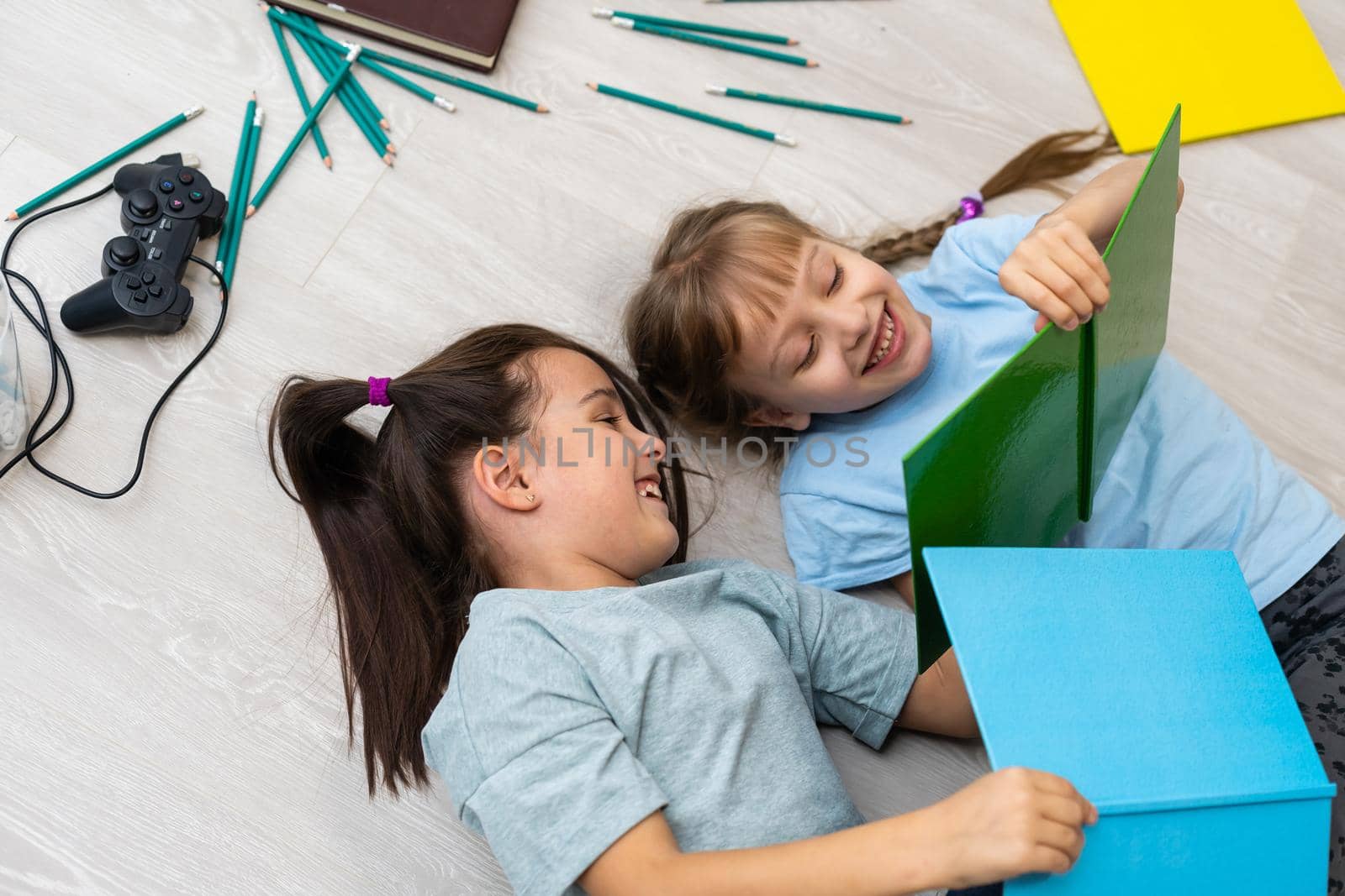 people, children, friends, literature and friendship concept - two happy girls lying on floor and reading book at home