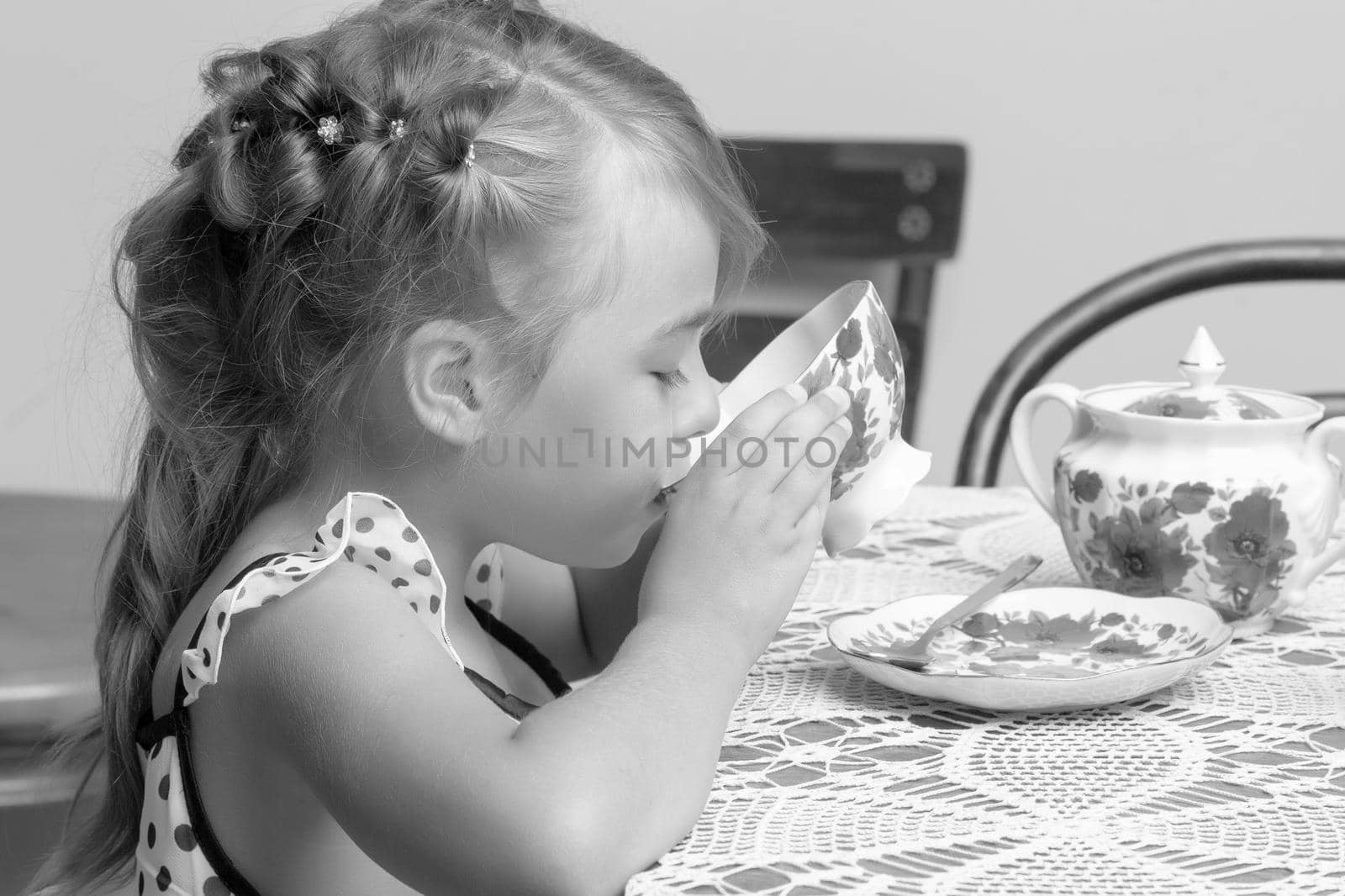 A little girl is drinking tea at the table. Stylized as a room of the fifties of last century. Retro style.
