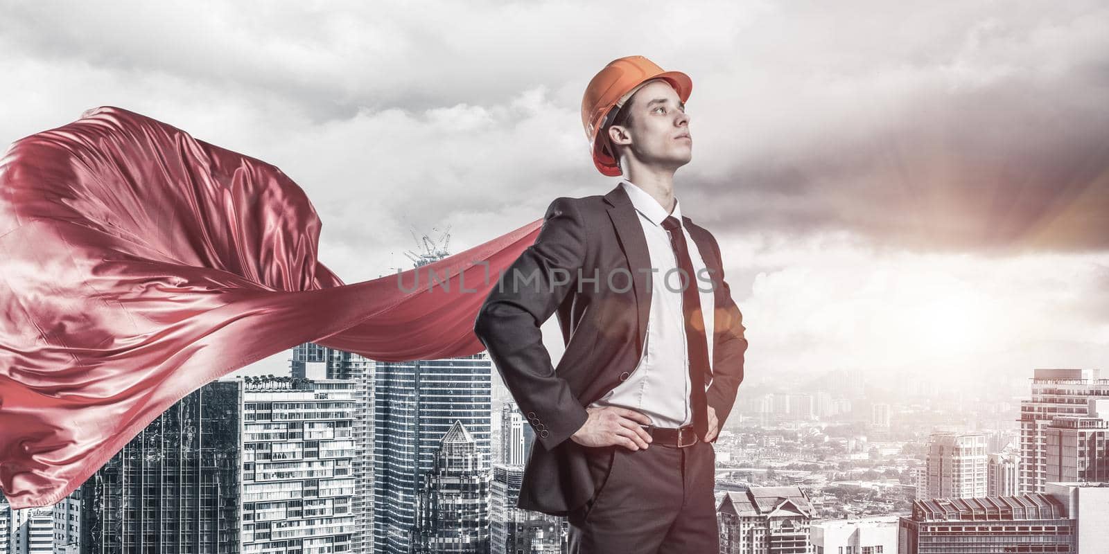 Confident engineer man in helmet and red cape against modern cityscape background