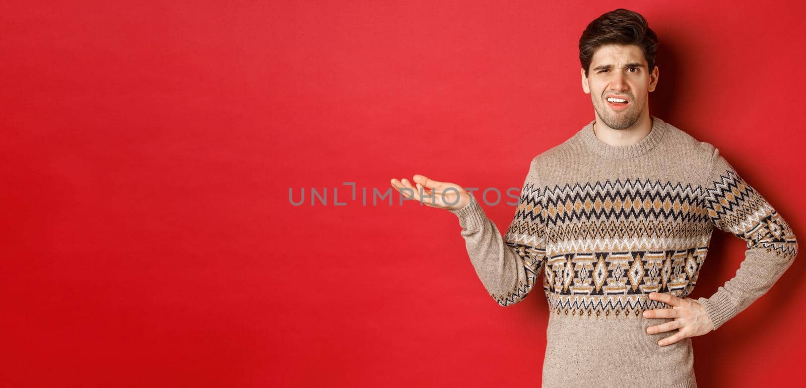 Image of confused and disappointed handsome man, complaining about christmas party, raising hand and looking bothered, standing over red background by Benzoix