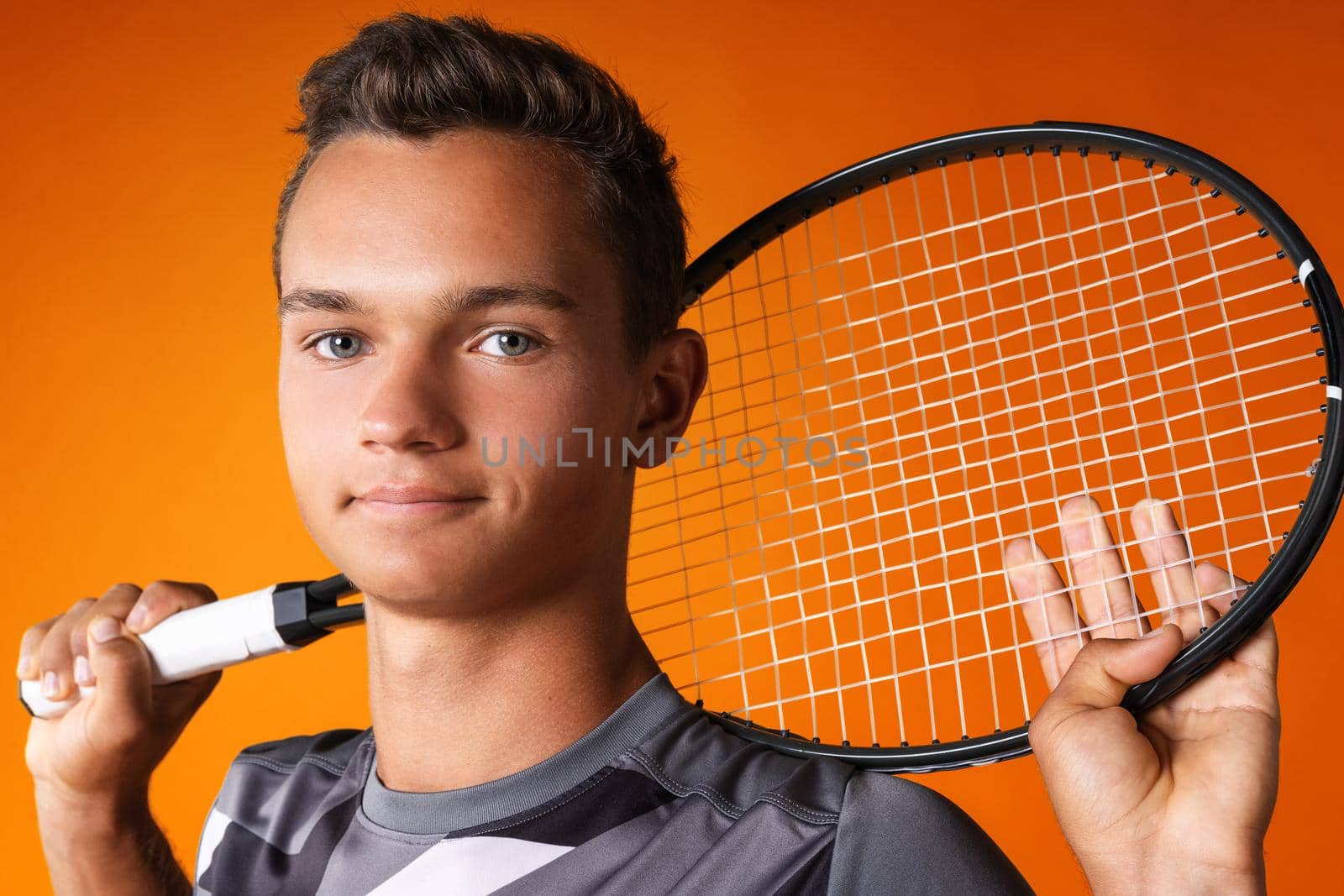 Portrait of a young man tennis player on orange background close up