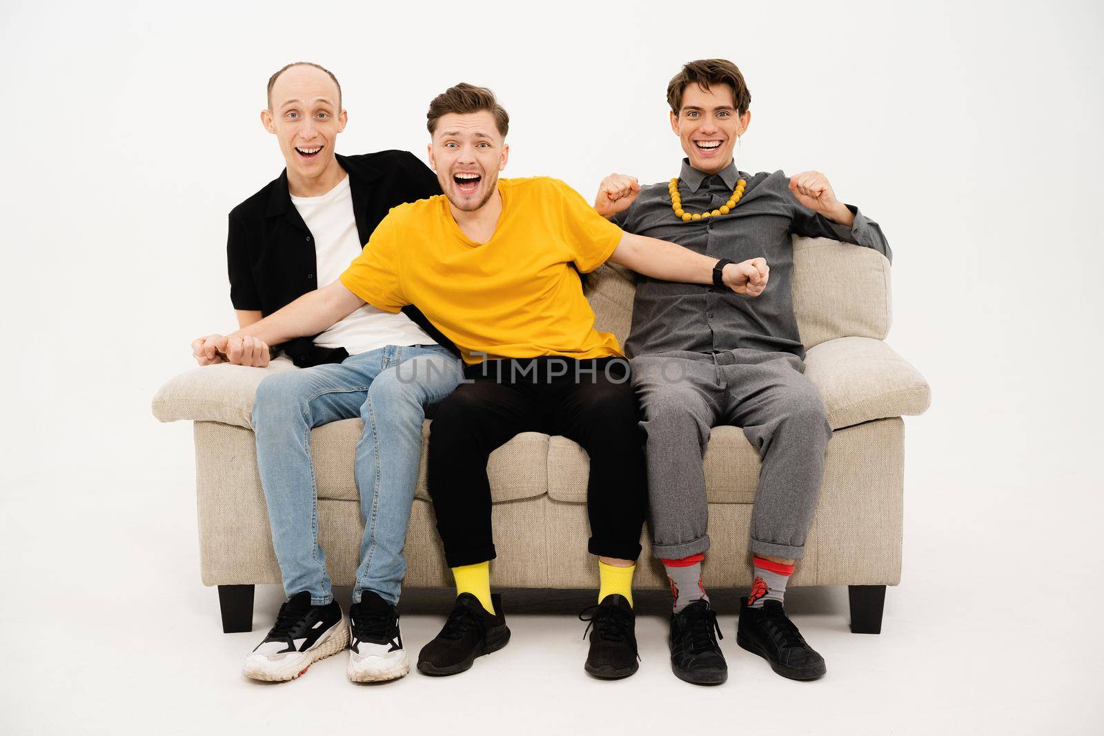 Watching a championship game on tv tree friends sitting on a white sofa isolated on white background. Guy reacts to winning or a lose. Sports tv concept.