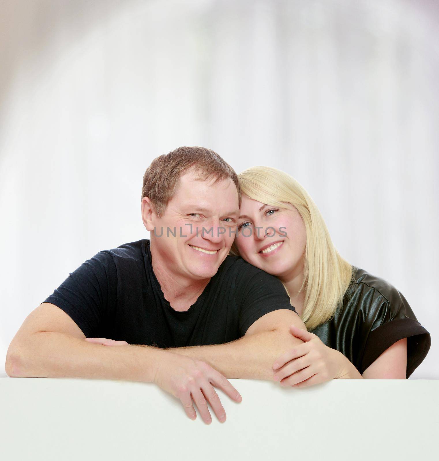 A man and a woman tenderly hugging each other. Peeping over white banner.