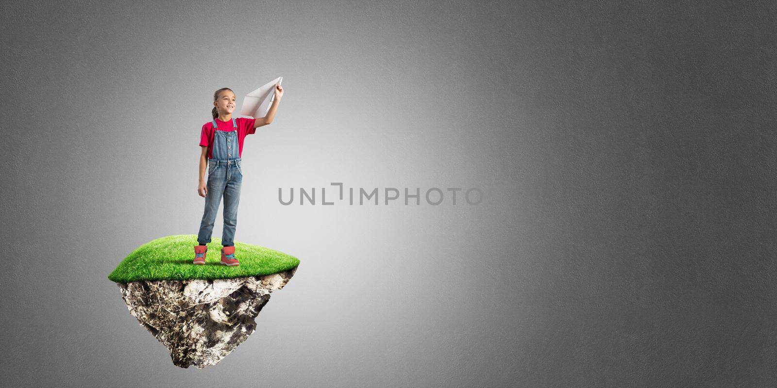 Cute kid girl standing on flying island throwing paper plane