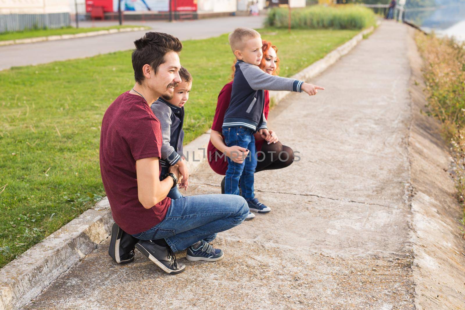 Parenthood, childhood and family concept - Parents and two male children walking at the park and looking on something by Satura86