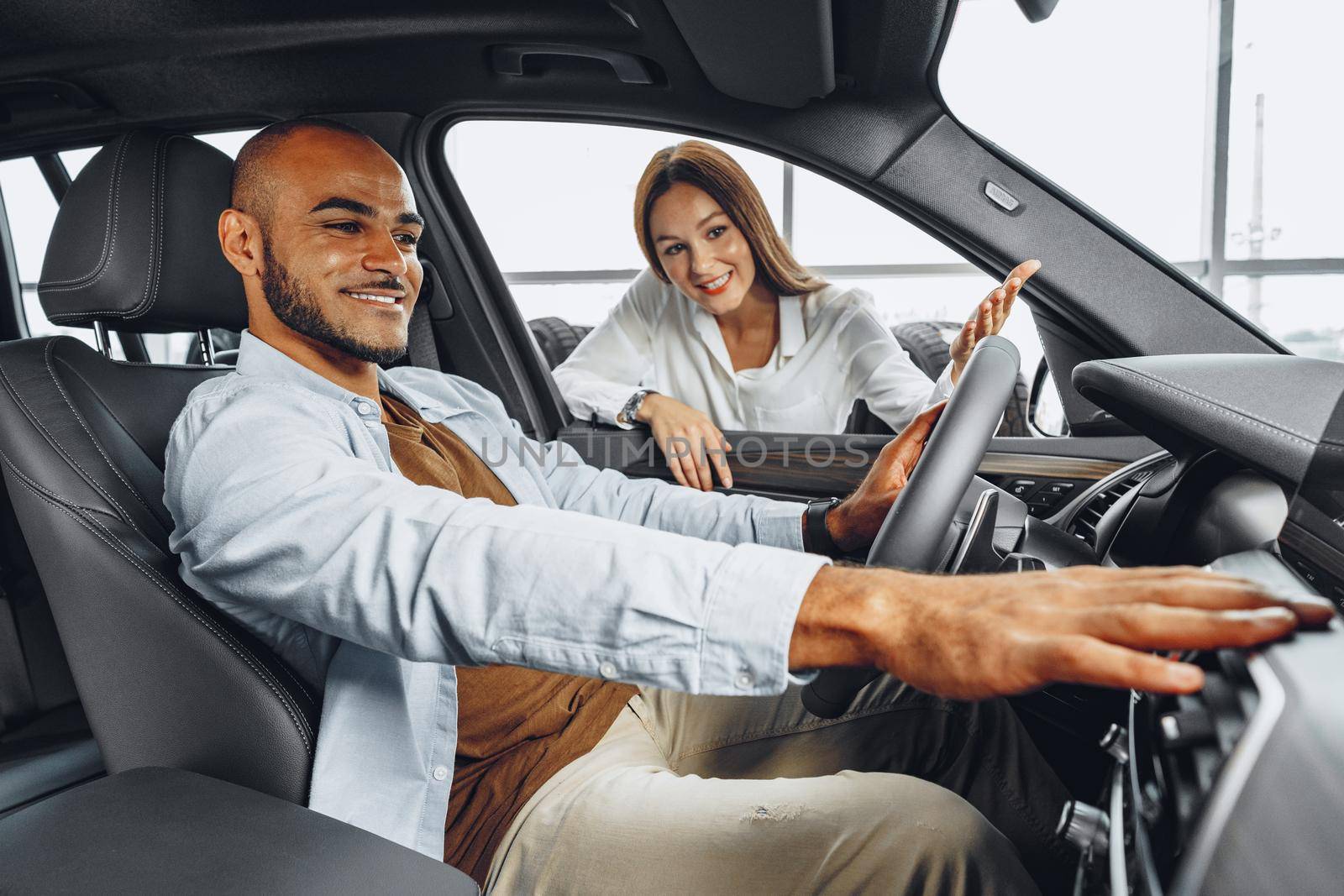 Young attractive caucasian woman salesperson in car showroom showing a car to her male African American client