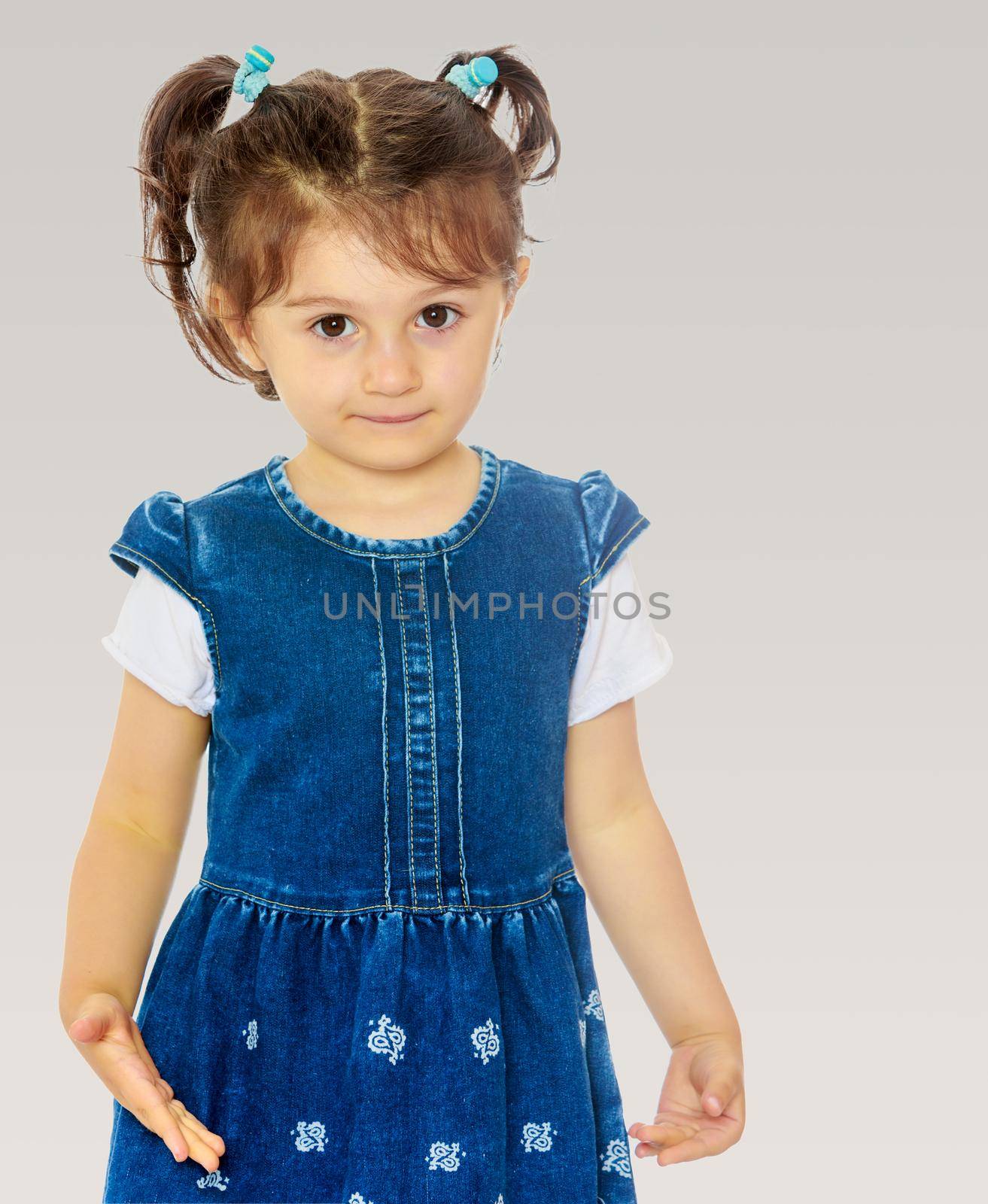 Cute little girl with short pigtails on the head, in a blue dress with short sleeves. Close-up.On a gray background.