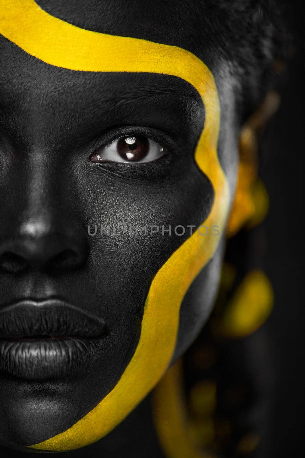 Face art. Woman with black and yellow body paint. Young african girl with colorful bodypaint. An amazing afro american model with yellow makeup.