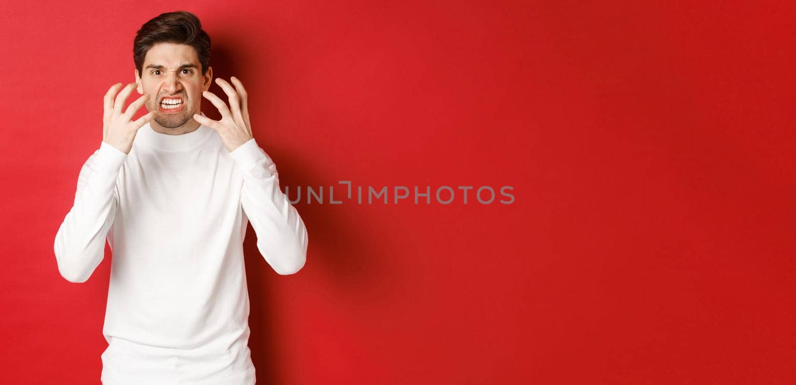 Image of angry and pissed-off man in white sweater, grimacing and shaking from rage, standing furious against red background by Benzoix