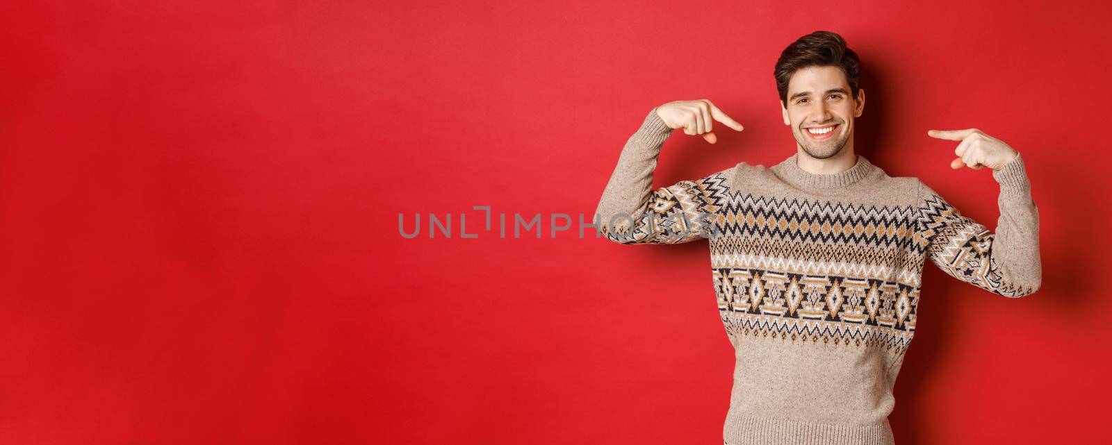 Concept of christmas celebration, winter holidays and lifestyle. Image of happy handsome man in xmas sweater pointing at himself and smiling, being secret santa, standing over red background by Benzoix