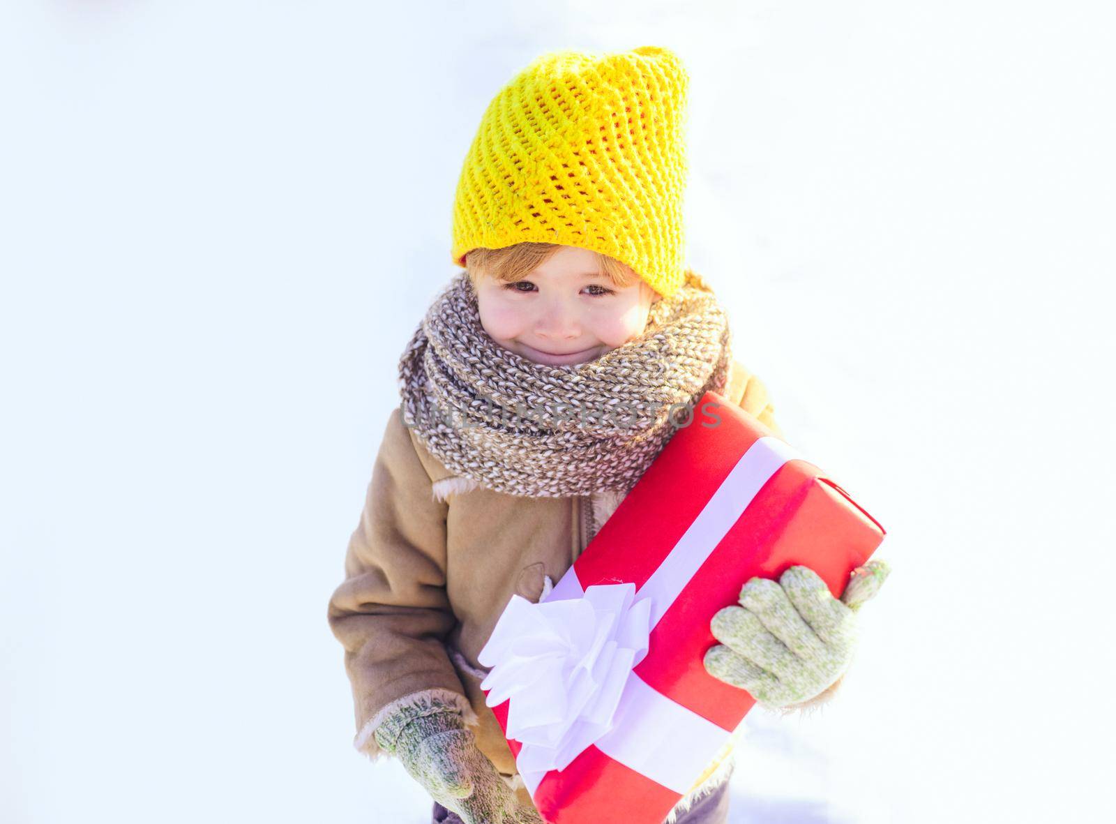 Winter child hold gift bow snow background. Cute boy in winter clothes hat and scarf close up. Happy new year and merry christmas