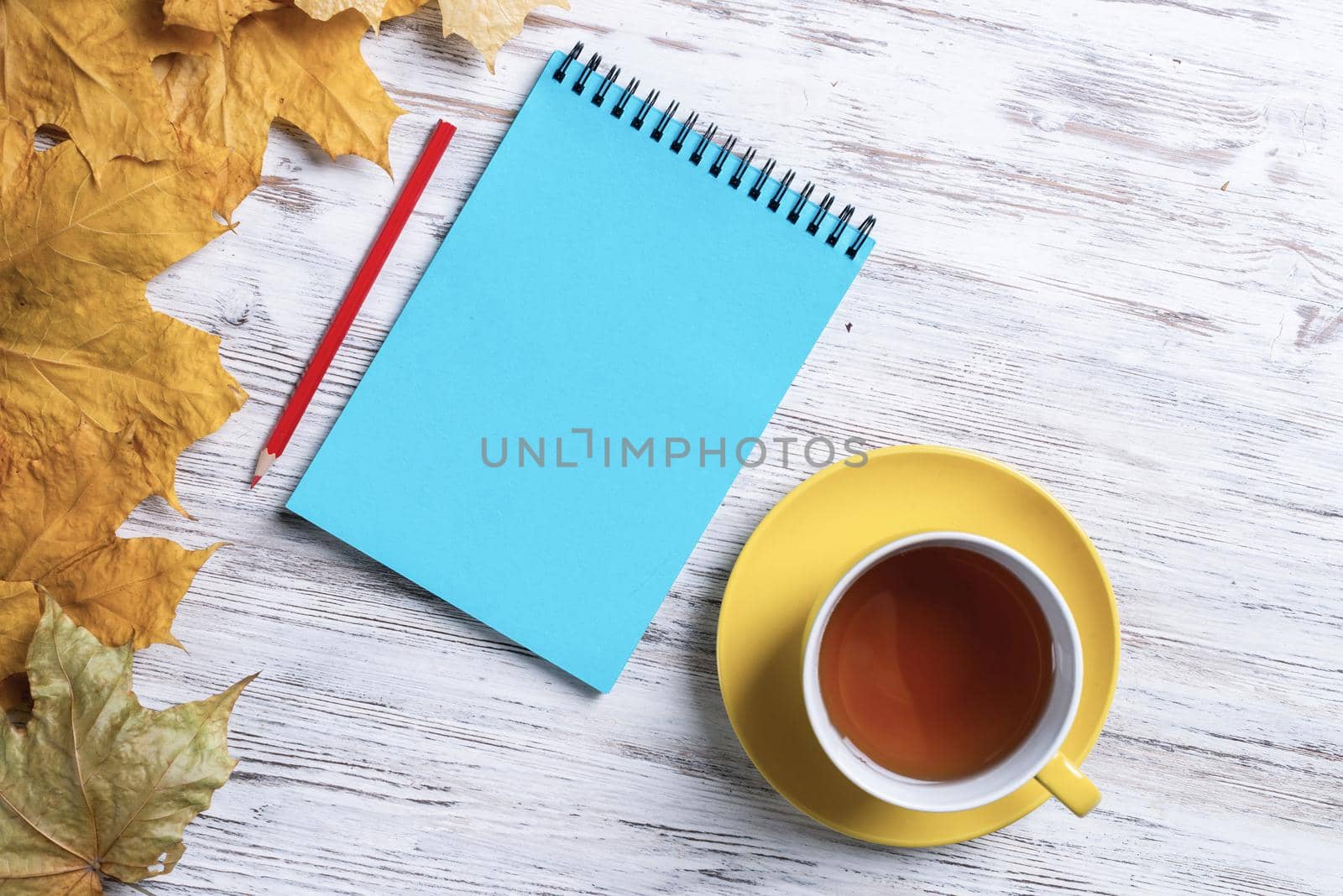 Flat lay autumn composition with cup of black tea and yellow autumn leaves. Time of tea break concept. Still life of hot drink and notepad with pen lies on vintage wooden desk with bright foliage.