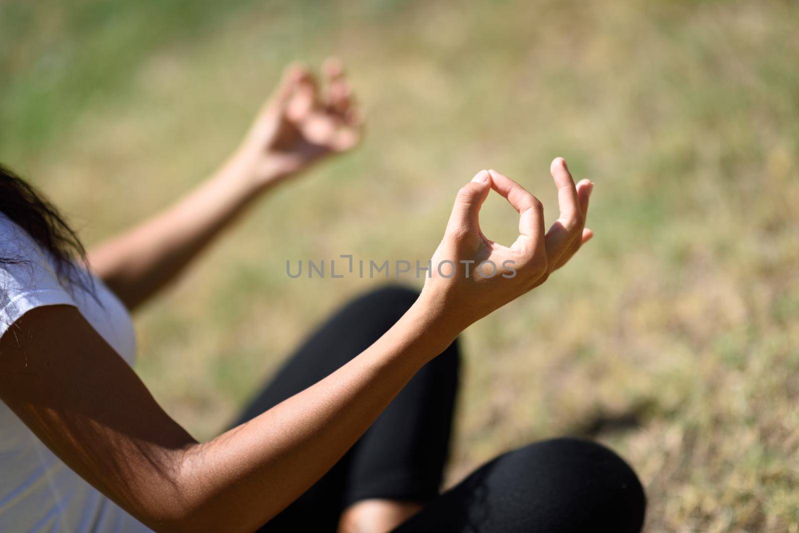 Young woman doing yoga on the grass of urban park. Female wearing sport clothes doing lotus figure in urban park.