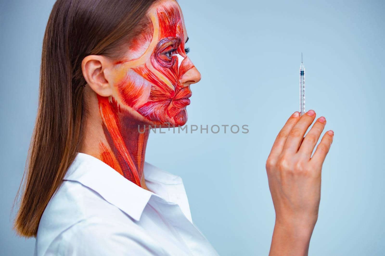 Cosmetic injection in the face. Young woman with half of face with muscles structure under skin. Model for medical training on a light background. by MikeOrlov