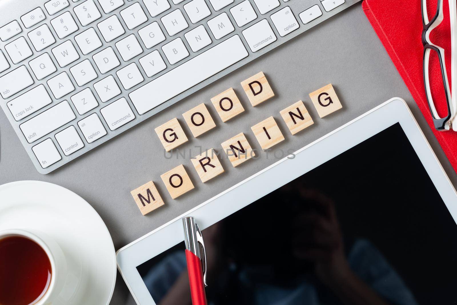 Good morning message with letters on wooden cubes. Still life of workspace with supplies. Flat lay grey surface with computer keyboard and cup of tea. Morning greeting phrase and motivation.