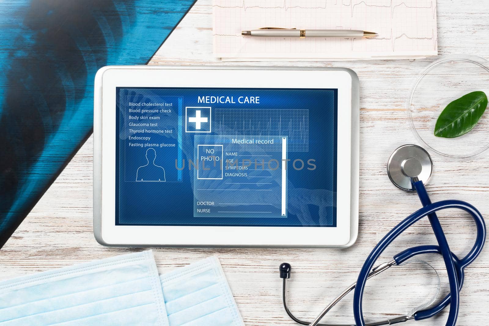 Laboratory patient examination in doctors office. Tablet computer with medical app interface on screen. Stethoscope, x-ray image and cardiogram on wooden desk. Medical diagnostics and examination