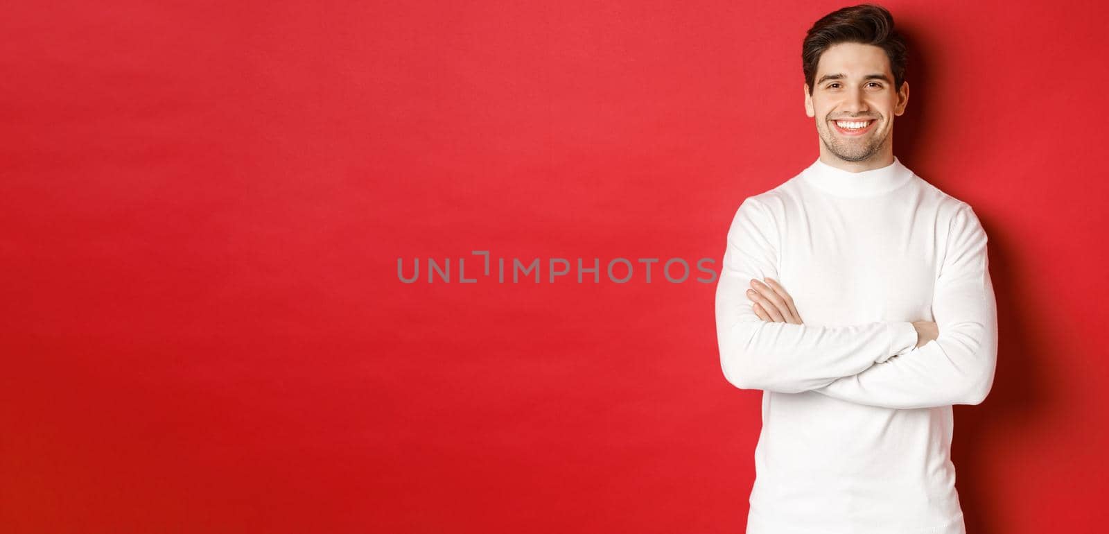 Concept of winter holidays, christmas and lifestyle. Portrait of confident good-looking man with bristle, wearing white sweater, cross arms on chest and smiling satisfied.